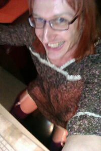 Yläviistosta otettu selfie. Istun tietokoneen ääressä jumppapallon päällä. Ylläni on lyhyt läpikuultava kukallinen ja pitsisomisteinen mekko ja sukkanauhat. Naama kiiltelee rasvaisena ja virnistän maanisesti.